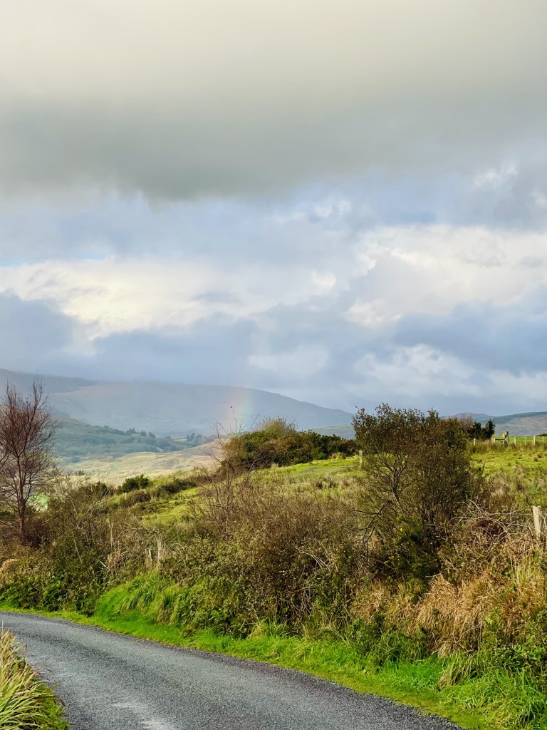 Ireland scenery with clouds and a rainbow in the distance.